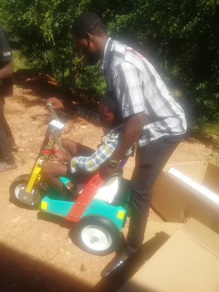 A RECOAT staff member helping a child onto an adapted mobility tricycle