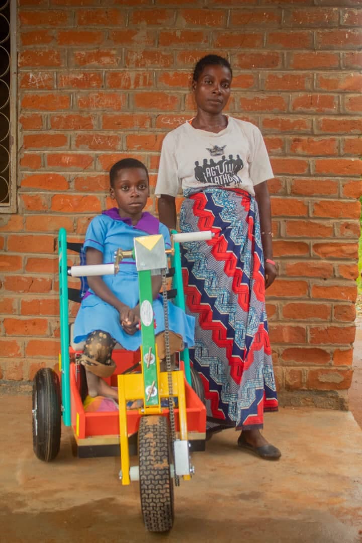 A schoolgirl with her adapted mobility tricycle, standing with her guardian