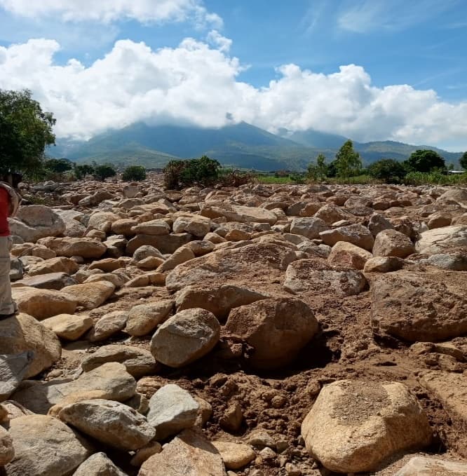 A field of boulders and debris left behind after the cyclone, with mountains in the background